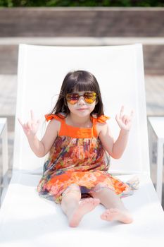 Beautiful portrait little girl asian of a smiling sitting at swimming pool, kid leisure and joyful wear glasses in outdoor.