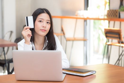 Beautiful young asian woman holding a credit card and shopping online with using laptop computer at cafe, girl payment on notebook to internet, business ecommerce and lifestyle concept.
