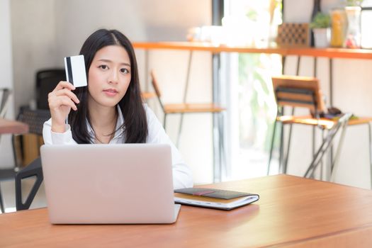 Beautiful young asian woman holding a credit card and shopping online with using laptop computer at cafe, girl payment on notebook to internet, business ecommerce and lifestyle concept.