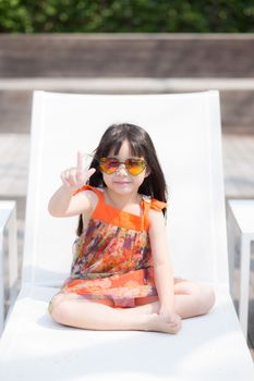 Beautiful portrait little girl asian of a smiling sitting at swimming pool, kid leisure and joyful wear glasses in outdoor.