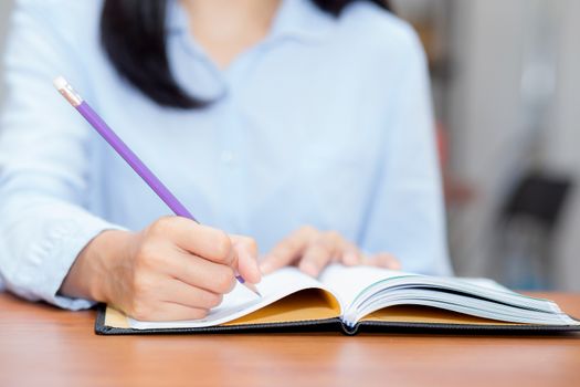 Closeup hand of asian young woman writing on notebook on table, girl work at coffee shop, freelance girl with paperwork message on note, education concept.