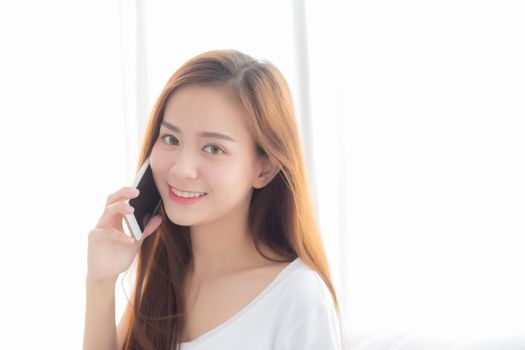 Beautiful of portrait young asian woman talking smart mobile phone and smile standing at curtain background on bedroom, girl calling telephone, communication concept.