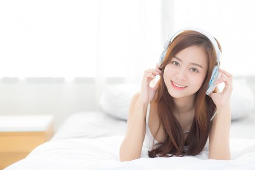Beautiful asian young woman enjoy listen music with headphone while lying in bedroom, relax girl with earphone internet online, leisure and technology concept.