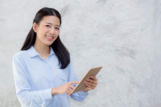 Beautiful young asian woman touch tablet computer and smile standing on cement background, freelancer girl with social media online, communication concept.