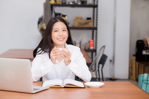 Beautiful asian young woman working online on laptop and drink coffee sitting at coffee shop, professional female freelancer using notebook computer with connect to internet for distance job.