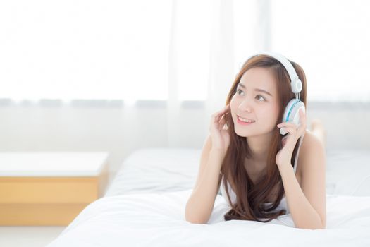 Beautiful asian young woman enjoy listen music with headphone while lying in bedroom, relax girl with earphone internet online, leisure and technology concept.