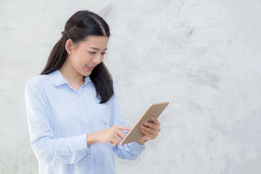 Beautiful young asian woman touch tablet computer and smile standing on cement background, freelancer girl with social media online, communication concept.