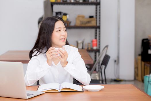 Beautiful asian young woman working online on laptop and drink coffee sitting at coffee shop, professional female freelancer using notebook computer with connect to internet for distance job.