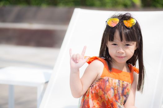 Beautiful portrait little girl asian of a smiling sitting at swimming pool, kid leisure and joyful wear glasses in outdoor.