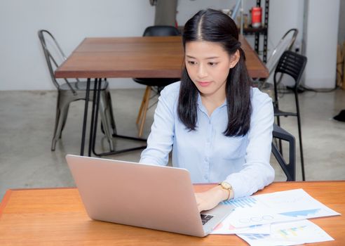 Beautiful of portrait asian young woman working with graph statistic paper on laptop sitting at coffee shop, professional female freelancer using notebook computer with report and analysis, business concept.