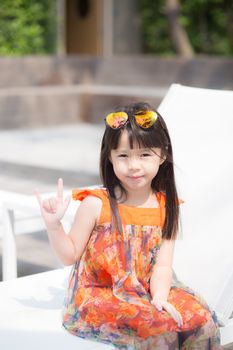 Beautiful portrait little girl asian of a smiling sitting at swimming pool, kid leisure and joyful wear glasses in outdoor.