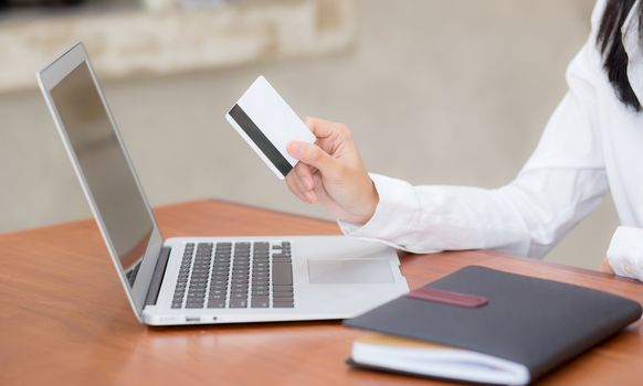 Beautiful young asian woman holding a credit card and shopping online with using laptop computer at cafe, girl payment on notebook to internet, business ecommerce and lifestyle concept.