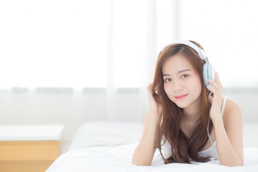 Beautiful asian young woman enjoy listen music with headphone while lying in bedroom, relax girl with earphone internet online, leisure and technology concept.