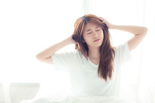 Beautiful young asian woman stretch and relax in bed after wake up morning at bedroom, back view, new day and resting for wellness, lifestyle concept.