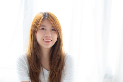 Portrait of beautiful young asian woman standing the window and smile while wake up with sunrise at morning, lifestyle and relax concept.