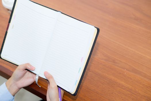 closeup woman hand writing on notebook on wooden table, girl work with paper at coffee shop, top view; freelance business concept.