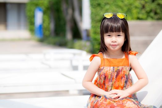 Beautiful portrait little girl asian of a smiling sitting at swimming pool, kid leisure and joyful wear glasses in outdoor.