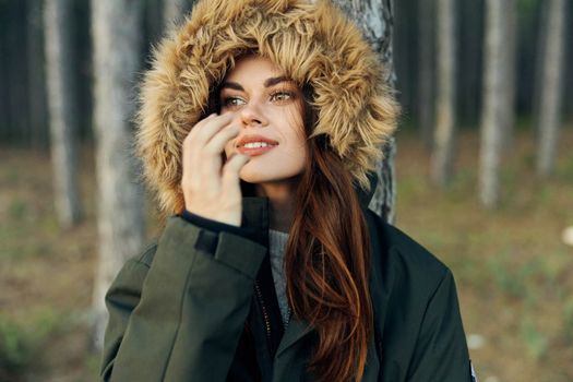 woman in autumn forest on warm jacket with a hood holds her hand near her face. High quality photo