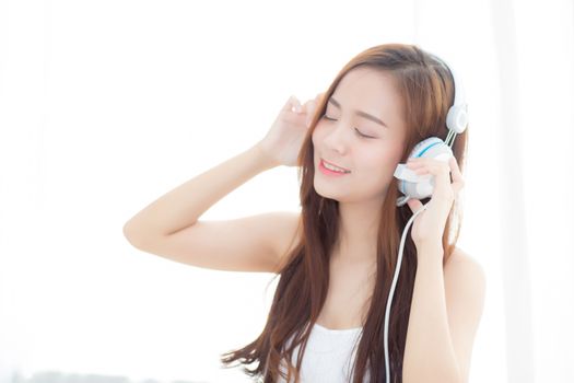 Beautiful asian young woman enjoy listen music with headphone while sitting in bedroom, relax girl with earphone internet online, leisure and technology concept.