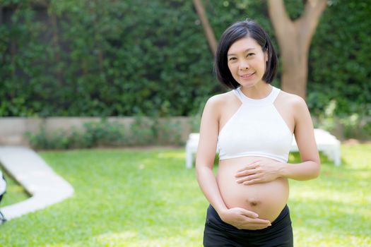 Beautiful pregnant of portrait asian young woman relax in the park, girl with belly standing on grass and yoga exercise for wellness, copy space.