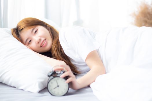 Beautiful of portrait asian young woman turn off alarm clock in morning, wake up for sleep with alarm clock, relax and lifestyle concept.