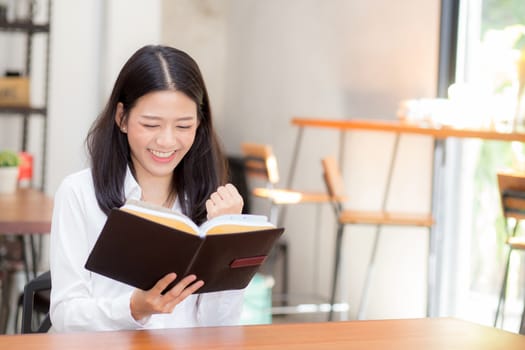 Beautiful of portrait business asian young woman reading on notebook with success on table, girl looking note excited at coffee shop, freelance and education concept.