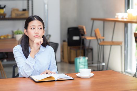 Beautiful of portrait business asian young woman thinking idea and writing on notebook on table, girl work at coffee shop, freelance business concept.