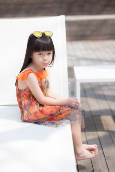 Beautiful portrait little girl asian of a smiling sitting at swimming pool, kid leisure and joyful wear glasses in outdoor.