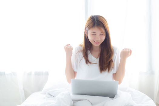 Beautiful happiness young asian woman using laptop work with success on bed in the home, girl and notebook shopping online with glad, communication concept.