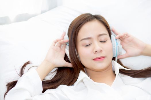 Beautiful asian young woman enjoy listen music with headphone while lying in bedroom, relax girl with earphone internet online, leisure and technology concept.