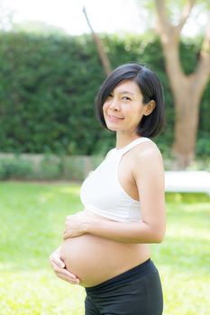 Beautiful pregnant of portrait asian young woman relax in the park, girl with belly standing on grass and yoga exercise for wellness, copy space.