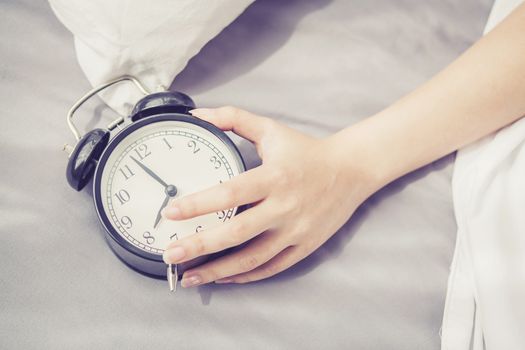 closeup asian young woman turn off alarm clock in good morning, wake up for sleep with  girl holding alarm clock, time and lifestyle concept.