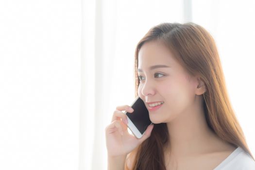 Beautiful of portrait young asian woman talking smart mobile phone and smile standing at curtain background on bedroom, girl calling telephone, communication concept.