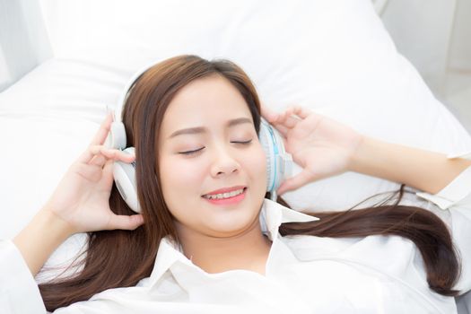 Beautiful asian young woman enjoy listen music with headphone while lying in bedroom, relax girl with earphone internet online, leisure and technology concept.