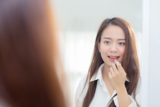 Beauty of portrait of young asian woman at the mirror holding and looking a makeup lipstick, Beautiful girl beauty fashion at the room, lifestyle concept.