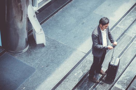 Asian elegant businessman wear suit talking mobile phone while walking holding suitcase outdoor on street, young man contact with customer appointment, communication business concept.