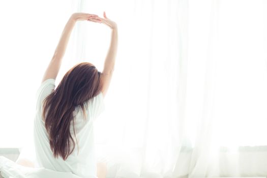Beautiful young asian woman stretch and relax in bed after wake up morning at bedroom, back view, new day and resting for wellness, lifestyle concept.