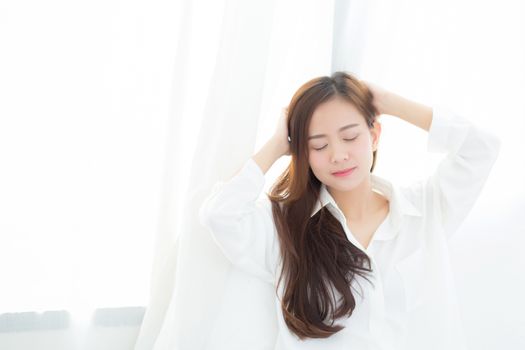 Portrait of beautiful young asian woman standing the window and smile while wake up with sunrise at morning, lifestyle and relax concept.