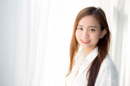 Portrait of beautiful young asian woman standing the window and smile while wake up with sunrise at morning, lifestyle and relax concept.
