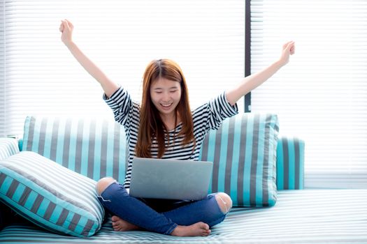 Beautiful happiness portrait of young asian woman using laptop work with success on sofa in the home, girl and notebook internet online with glad, communication concept.