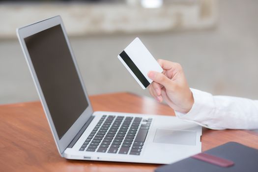 Beautiful young asian woman holding a credit card and shopping online with using laptop computer at cafe, girl payment on notebook to internet, business ecommerce and lifestyle concept.