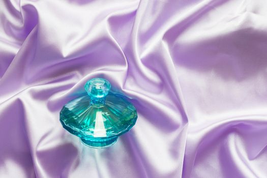 Perfume bottle on lilac silk folded fabric background. Luxery Scent fragrance cosmetic beauty product.