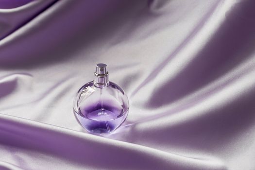 Perfume bottle on lilac silk folded fabric background. Luxery Scent fragrance cosmetic beauty product.