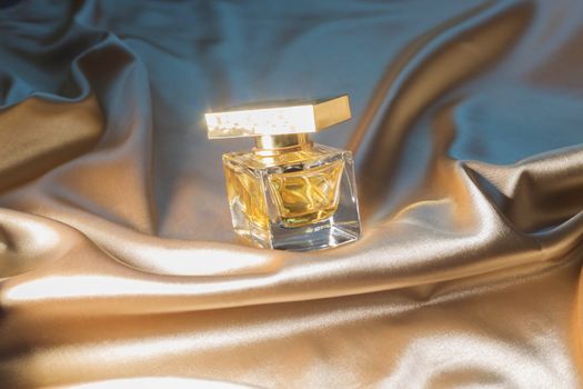 .Perfume bottle on gold folded silk fabric background. Luxery Scent fragrance cosmetic beauty product.