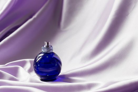 Perfume bottle on lilac silk folded fabric background. Luxery Scent fragrance cosmetic beauty product.