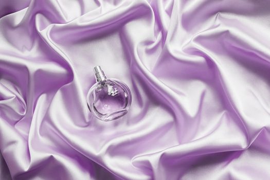 Perfume bottle on lilac silk folded fabric background. Luxery Scent fragrance cosmetic beauty product.