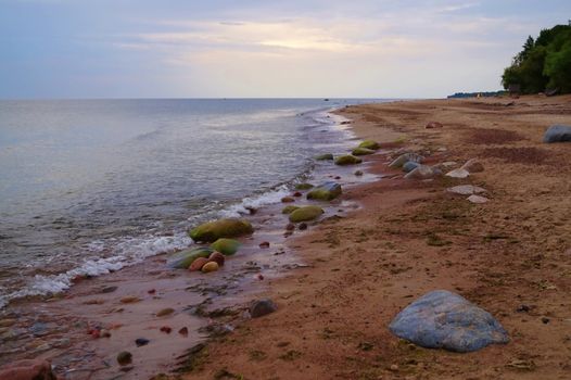 Calm sea lapping on a beach with red sand and scattered rocks in evening light in a low angle view