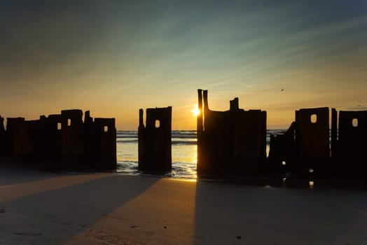 Ruined walls of a building at the edge of the ocean silhouetted against a colorful marine sunset wit orange sky and sunburst