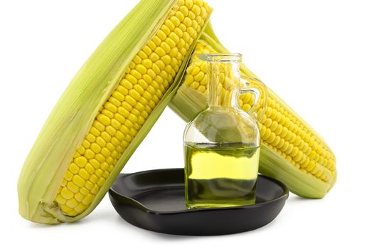 Corn oil in decanter in the cast iron skillet and fresh corncobs next to the cast iron skillet isolated on white background with free copy space for text