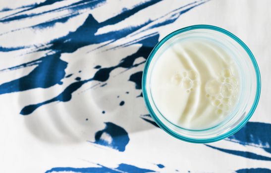 Blue glass with milk on table with colored tablecloth ,beautiful bubbles on milk surface